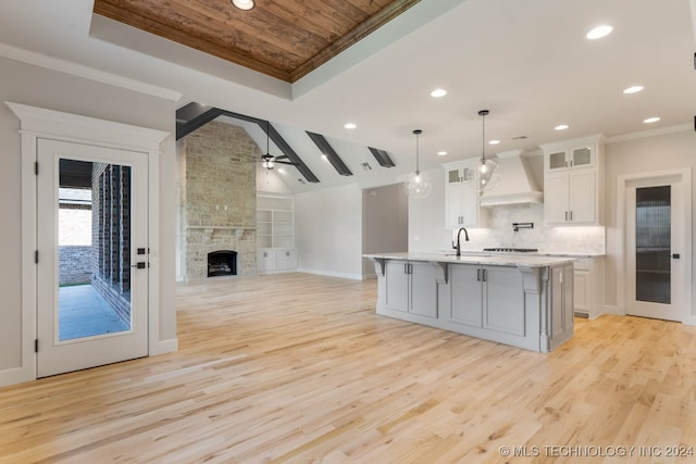 kitchen featuring a center island with sink, premium range hood, white cabinetry, light hardwood / wood-style flooring, and decorative light fixtures