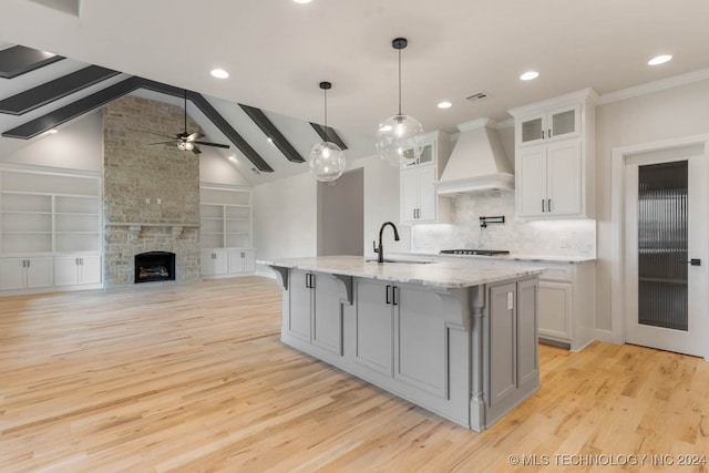 kitchen with white cabinets, premium range hood, light wood-type flooring, lofted ceiling with beams, and sink