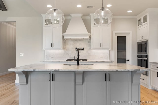 kitchen with a center island with sink, custom exhaust hood, white cabinets, and pendant lighting