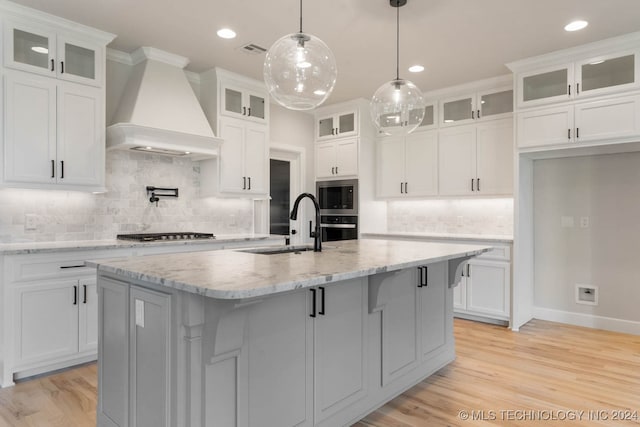 kitchen with custom range hood, decorative backsplash, an island with sink, and white cabinets