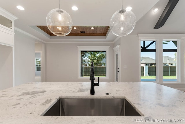 kitchen with light stone counters, a tray ceiling, sink, and decorative light fixtures