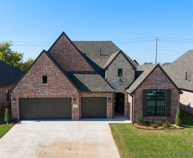 french country home with driveway, a shingled roof, an attached garage, a front yard, and brick siding