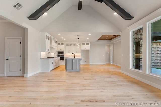 kitchen featuring a kitchen island with sink, light hardwood / wood-style flooring, decorative light fixtures, and white cabinetry