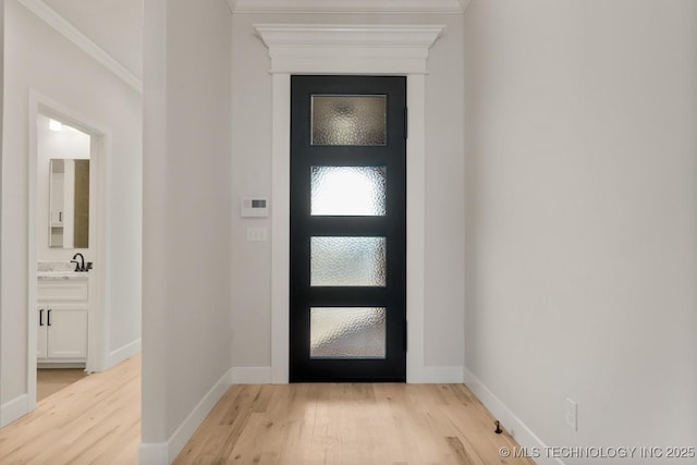 entryway with light wood finished floors, baseboards, and crown molding