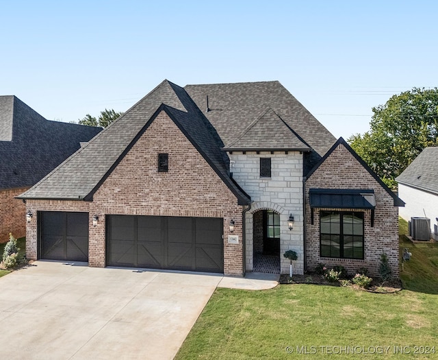 french provincial home with a garage, a front lawn, and central air condition unit