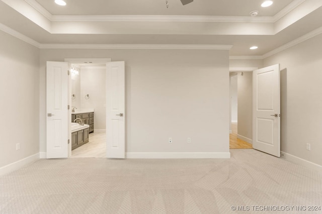 unfurnished bedroom with ensuite bathroom, a raised ceiling, ornamental molding, and light carpet