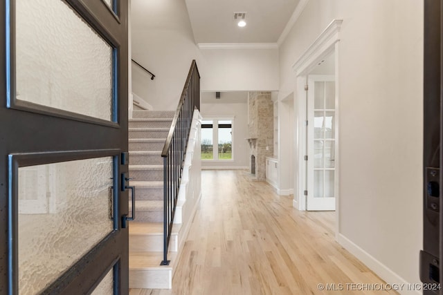 entryway featuring a stone fireplace, ornamental molding, and light wood-type flooring