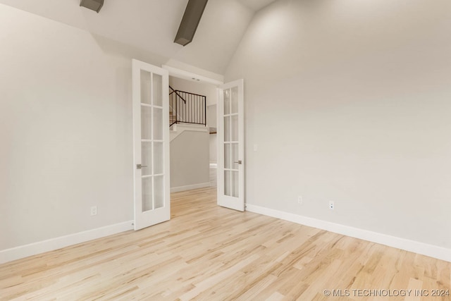 empty room with vaulted ceiling with beams, light wood-type flooring, and french doors