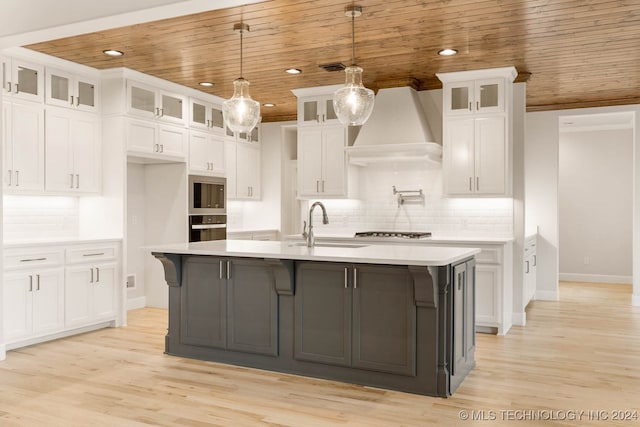 kitchen featuring appliances with stainless steel finishes, premium range hood, wood ceiling, white cabinets, and an island with sink