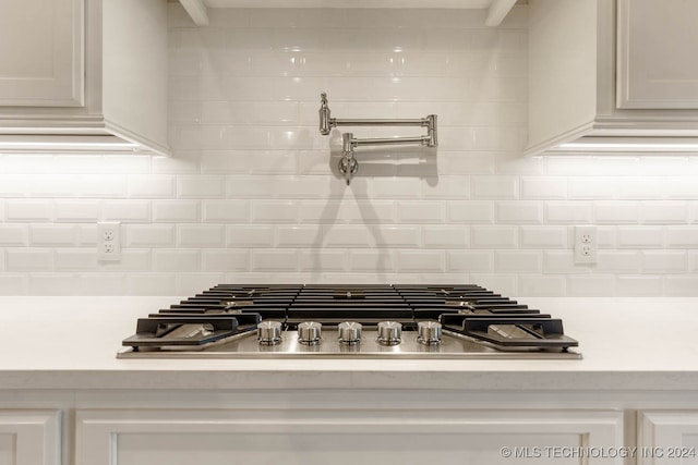 room details featuring white cabinets, decorative backsplash, and stainless steel gas stovetop