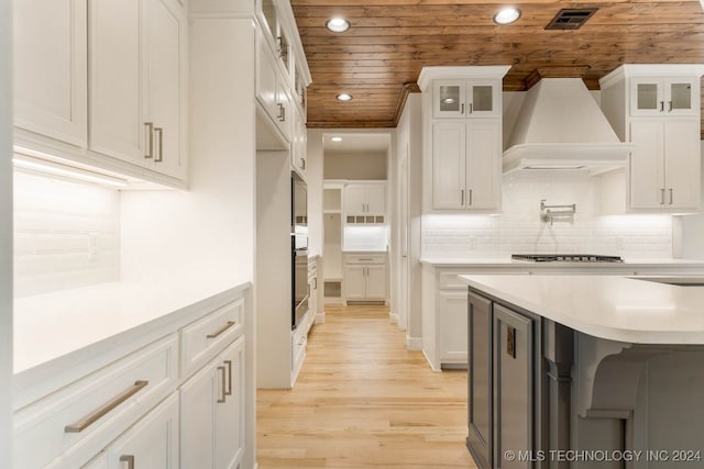 kitchen featuring wooden ceiling, stainless steel gas cooktop, white cabinets, custom range hood, and light wood-type flooring