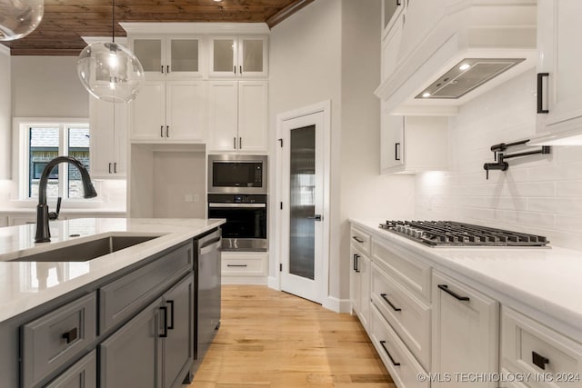 kitchen featuring light wood-type flooring, hanging light fixtures, white cabinetry, and sink