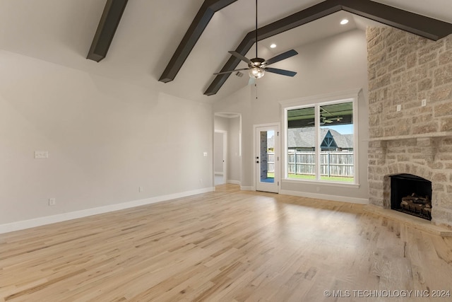 unfurnished living room featuring light wood-type flooring, beamed ceiling, high vaulted ceiling, a stone fireplace, and ceiling fan