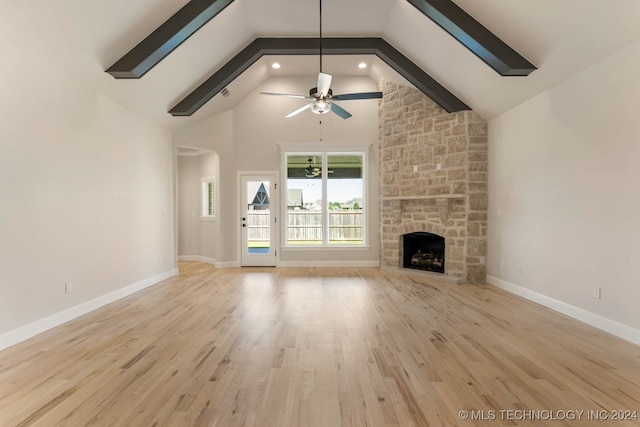 unfurnished living room featuring light hardwood / wood-style floors, high vaulted ceiling, a stone fireplace, beamed ceiling, and ceiling fan