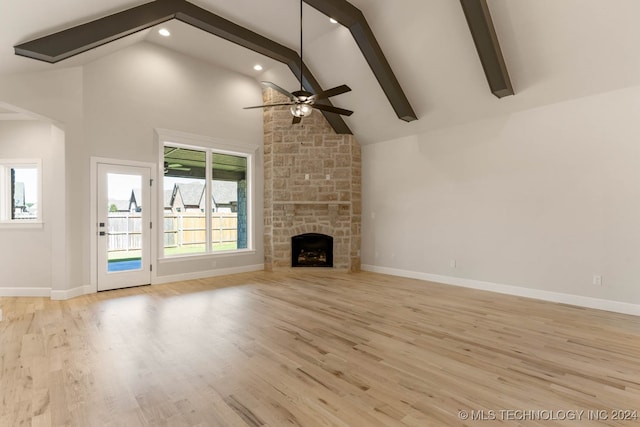 unfurnished living room featuring ceiling fan, beamed ceiling, a stone fireplace, high vaulted ceiling, and light wood-type flooring