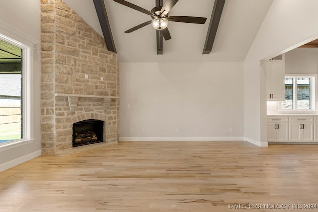 unfurnished living room featuring ceiling fan, beamed ceiling, high vaulted ceiling, a fireplace, and light hardwood / wood-style floors