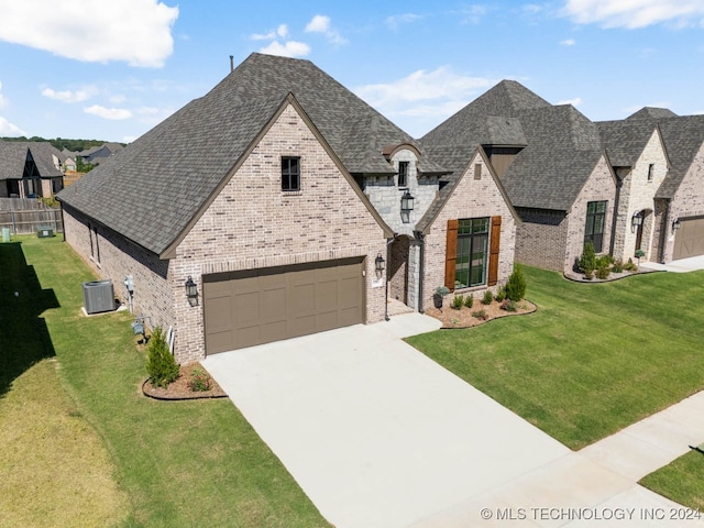 french country home featuring a garage, a front lawn, and central air condition unit