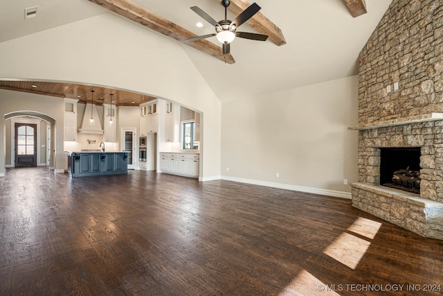 unfurnished living room featuring a stone fireplace, beamed ceiling, dark wood-type flooring, and high vaulted ceiling