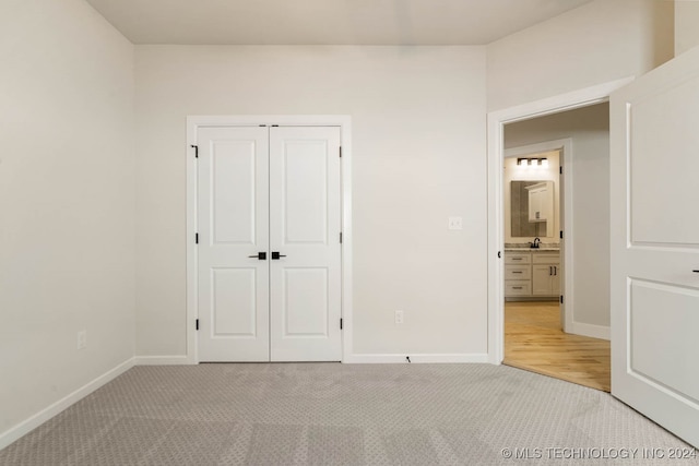 unfurnished bedroom with light carpet, a closet, and ensuite bath