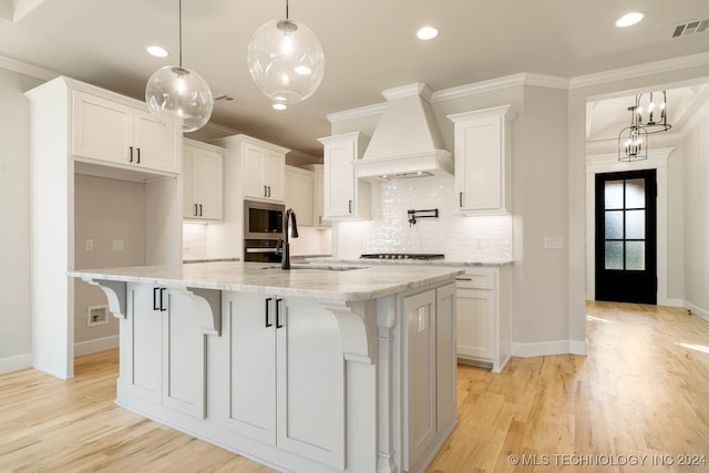 kitchen featuring white cabinetry, pendant lighting, custom exhaust hood, and a center island with sink