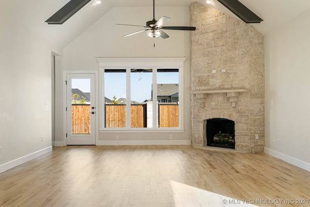 unfurnished living room featuring ceiling fan, high vaulted ceiling, light hardwood / wood-style floors, and a stone fireplace