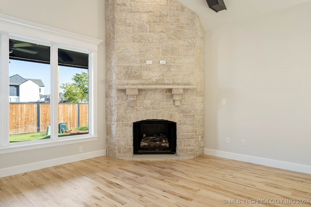 unfurnished living room featuring a stone fireplace, a healthy amount of sunlight, and wood-type flooring