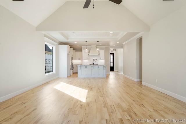 unfurnished living room featuring lofted ceiling, a raised ceiling, light hardwood / wood-style floors, and plenty of natural light