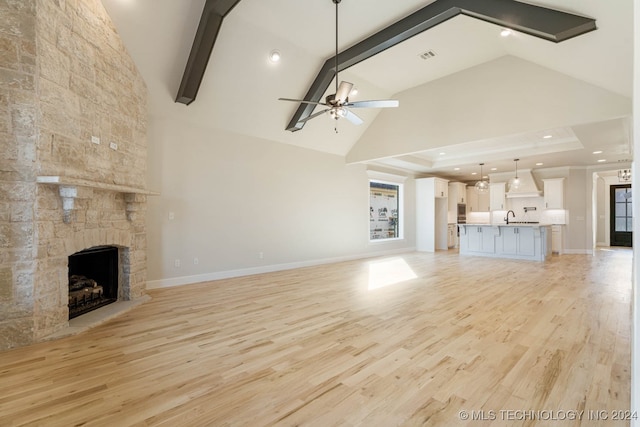 unfurnished living room with light hardwood / wood-style floors, ceiling fan, a stone fireplace, and beamed ceiling