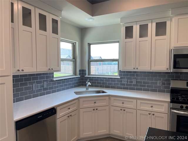 kitchen with appliances with stainless steel finishes, sink, backsplash, and white cabinetry