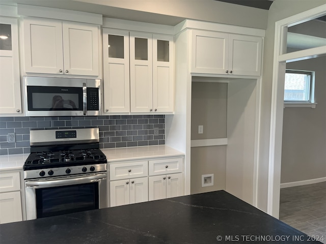 kitchen featuring stainless steel appliances, tasteful backsplash, dark stone counters, white cabinetry, and hardwood / wood-style floors