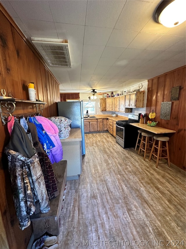 interior space with gas stove, sink, hardwood / wood-style floors, wooden walls, and refrigerator