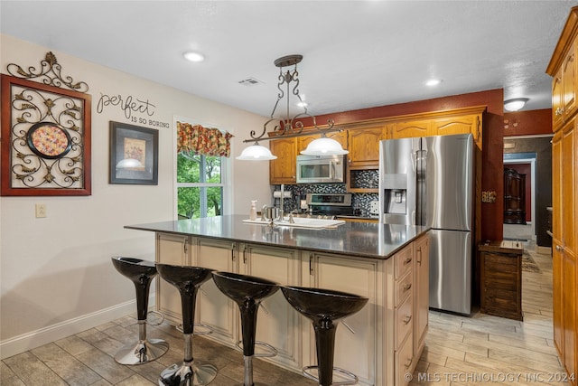 kitchen featuring appliances with stainless steel finishes, a kitchen breakfast bar, light hardwood / wood-style floors, hanging light fixtures, and an island with sink