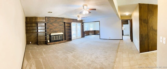 unfurnished living room featuring built in features, ceiling fan, a fireplace, a textured ceiling, and light colored carpet