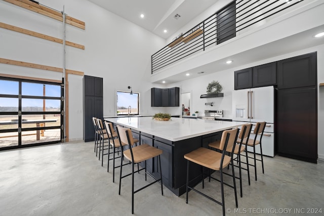 kitchen with high end white refrigerator, a towering ceiling, a kitchen bar, a spacious island, and stove