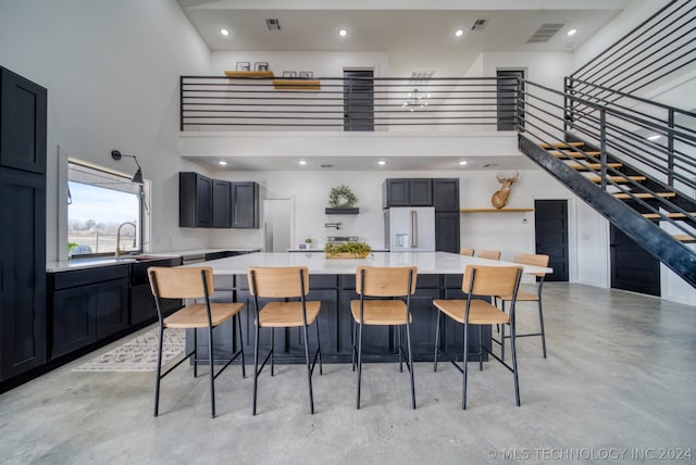 kitchen featuring white fridge with ice dispenser, a towering ceiling, a kitchen island, and a breakfast bar