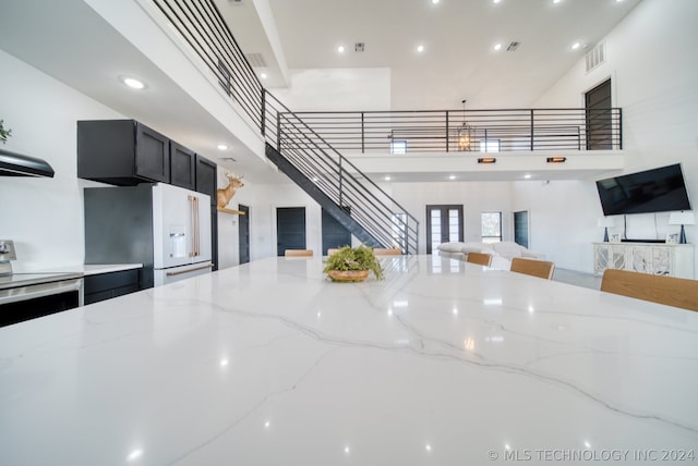 kitchen with white refrigerator with ice dispenser, a towering ceiling, range, and light stone counters