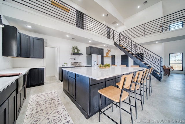 kitchen featuring white refrigerator with ice dispenser, a towering ceiling, a kitchen island, and a breakfast bar area