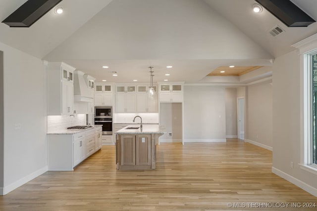 kitchen with white cabinets, a center island with sink, light hardwood / wood-style flooring, stainless steel appliances, and light stone countertops