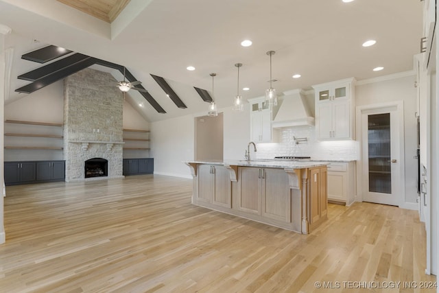 kitchen with an island with sink, white cabinetry, light hardwood / wood-style flooring, light stone countertops, and premium range hood