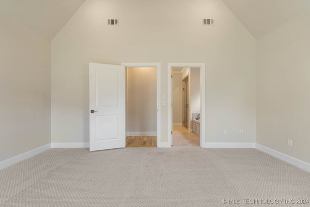 interior space with light colored carpet, connected bathroom, and high vaulted ceiling