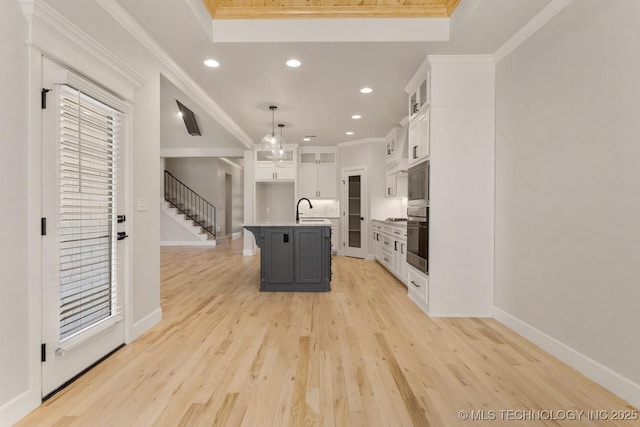 kitchen with light countertops, hanging light fixtures, a kitchen island with sink, a sink, and white cabinetry