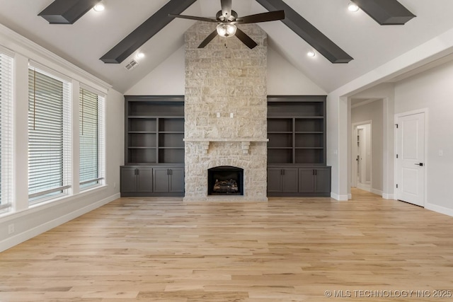 unfurnished living room featuring a ceiling fan, light wood-type flooring, beam ceiling, and a stone fireplace