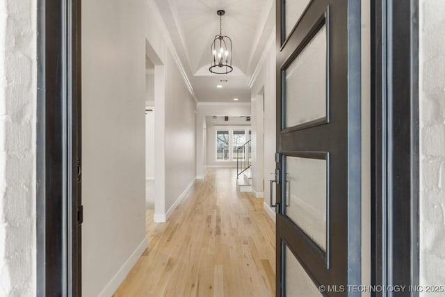 corridor with ornamental molding, light wood-style floors, baseboards, and an inviting chandelier