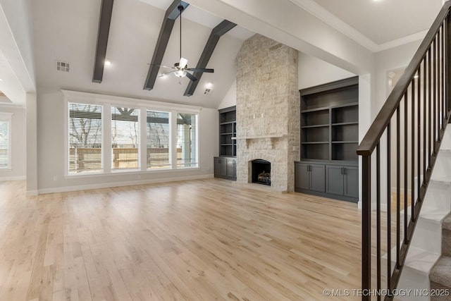 unfurnished living room featuring a fireplace, visible vents, stairway, light wood-type flooring, and beamed ceiling