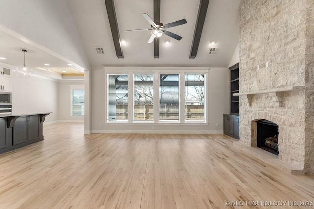 unfurnished living room featuring a wealth of natural light, a stone fireplace, light wood-style flooring, and visible vents