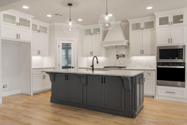 kitchen with a kitchen island with sink, glass insert cabinets, oven, and custom range hood