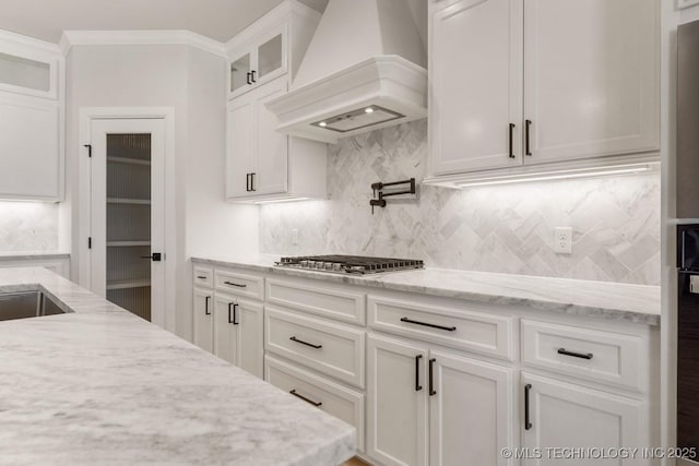 kitchen with light stone counters, premium range hood, white cabinets, glass insert cabinets, and stainless steel gas stovetop