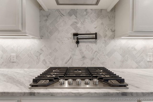 interior details with light stone countertops, tasteful backsplash, stainless steel gas cooktop, and white cabinets