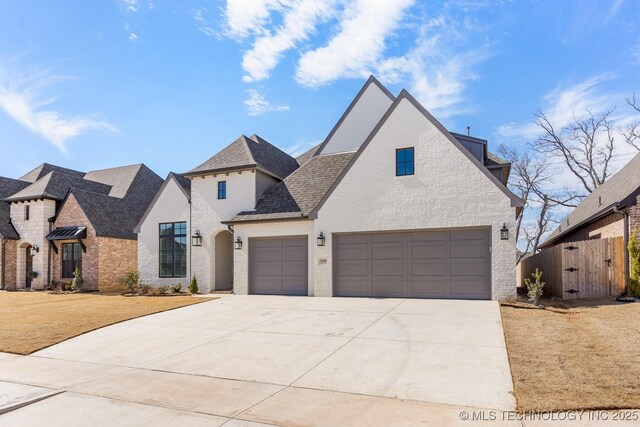 french country style house with driveway, roof with shingles, a gate, fence, and brick siding