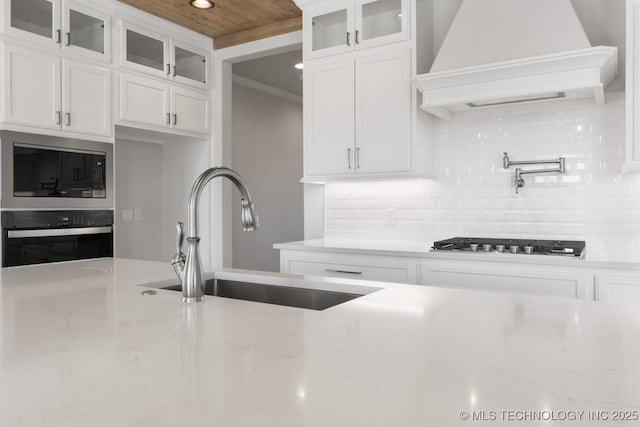 kitchen featuring backsplash, premium range hood, stainless steel appliances, and a sink